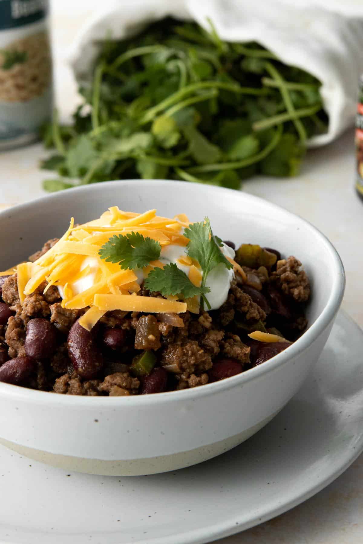 bowl of chili with toppings, cilantro in background