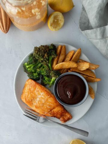 salmon filet, broccoli, potato wedges on plate with bowl of bbq sauce