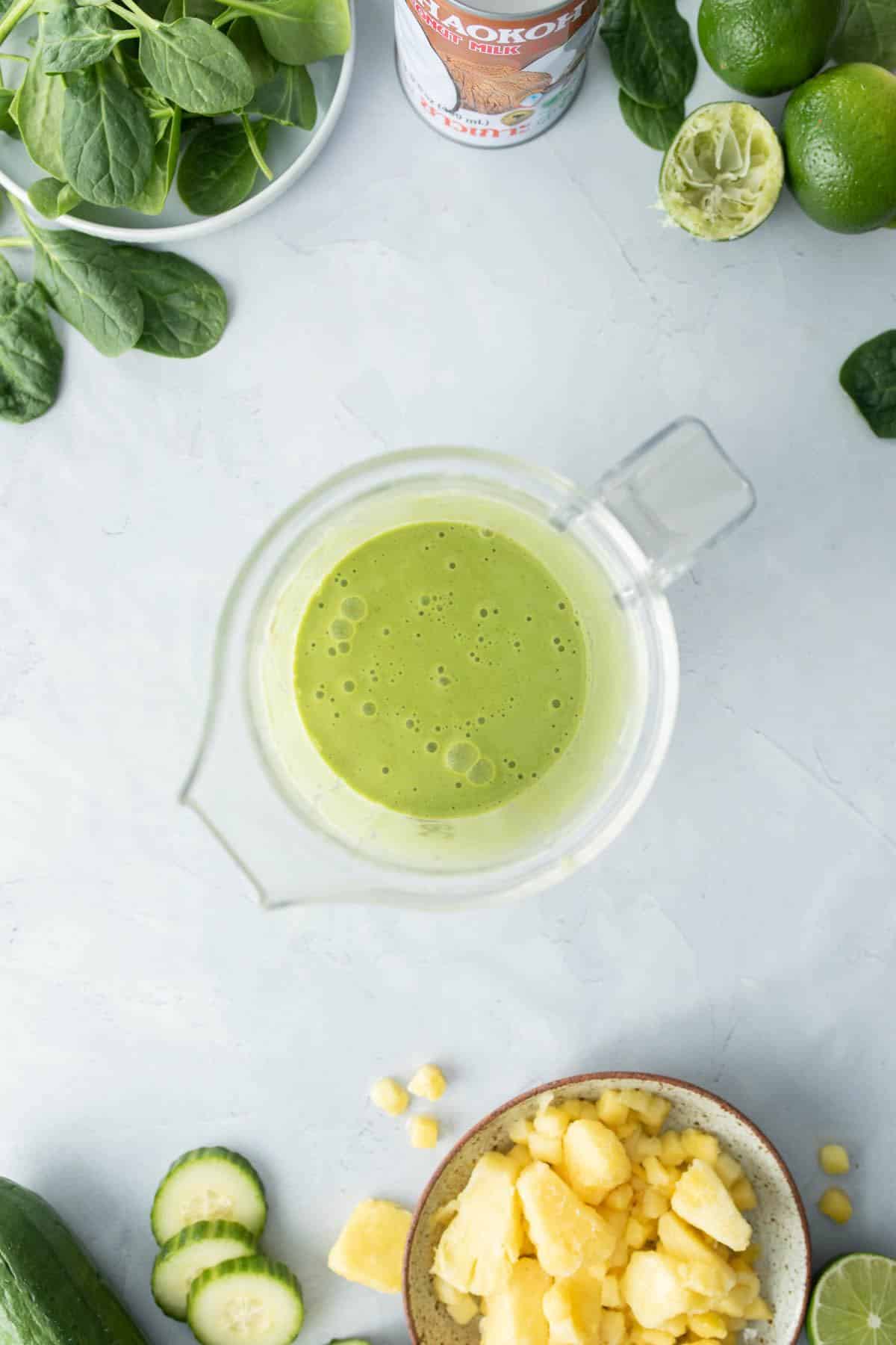 blender jar full of green smoothie, ingredients surrounding it