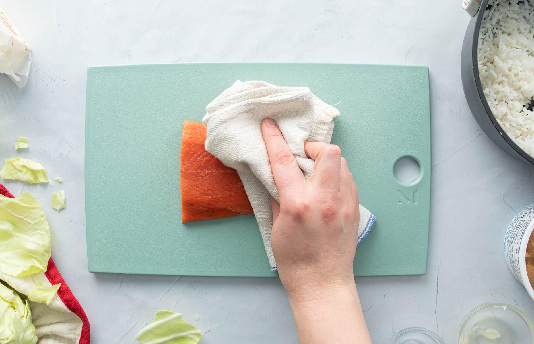 hand patting salmon dry with towel