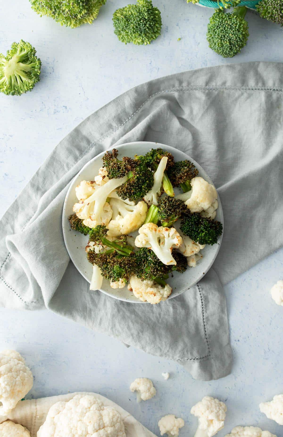 roasted broccoli and cauliflower on plate, raw vegetables around