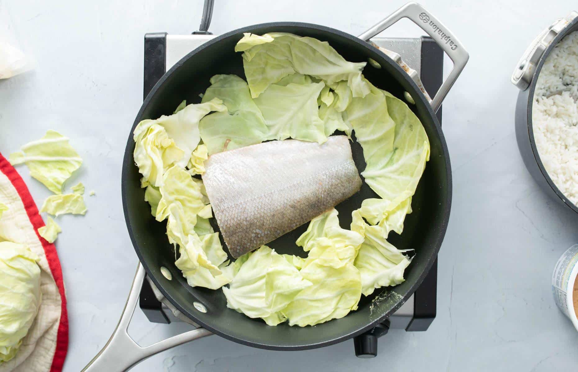 salmon, skin side up and cabbage cooking in pan