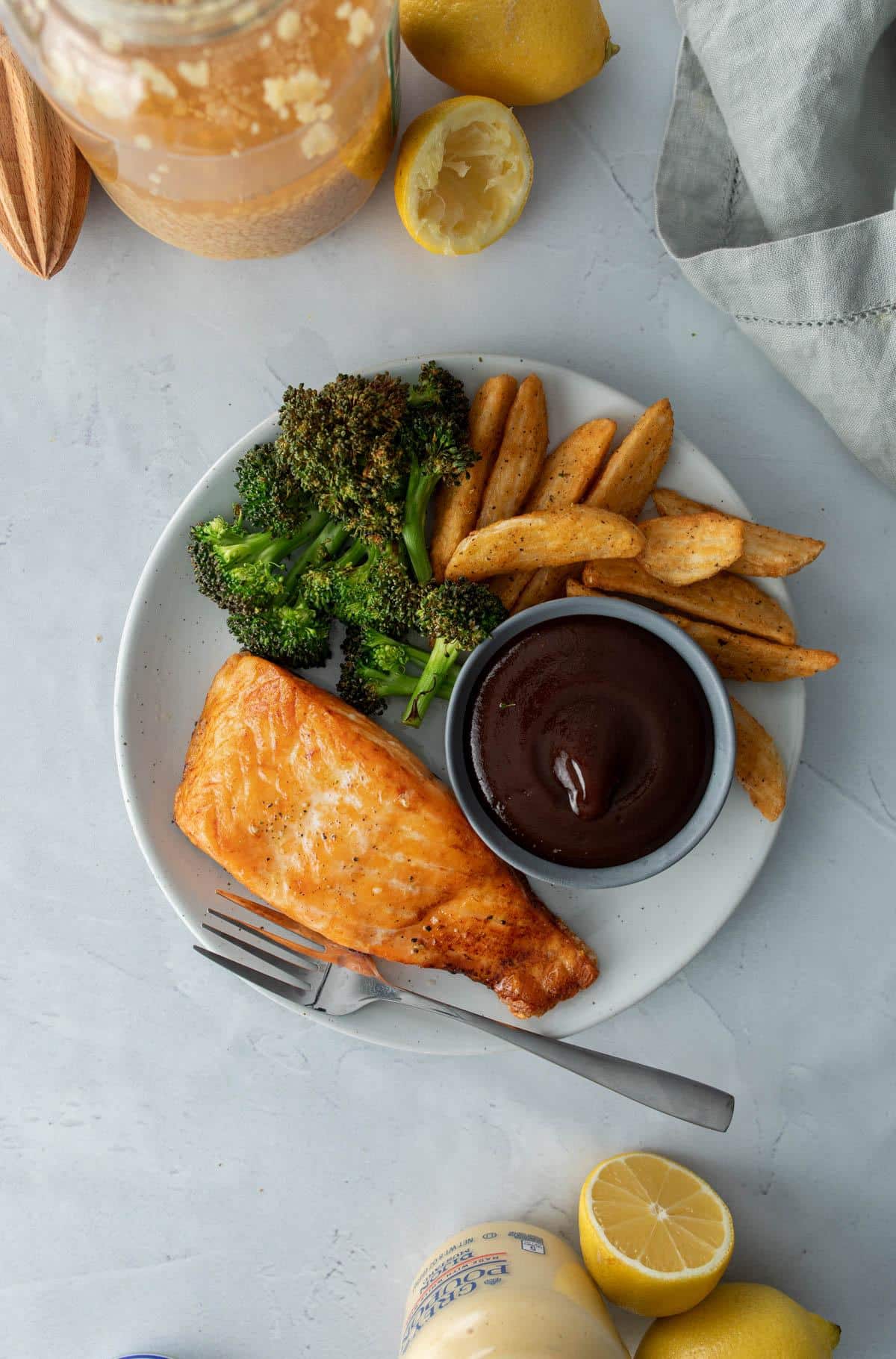 salmon filet, broccoli, potato wedges on plate with bowl of bbq sauce