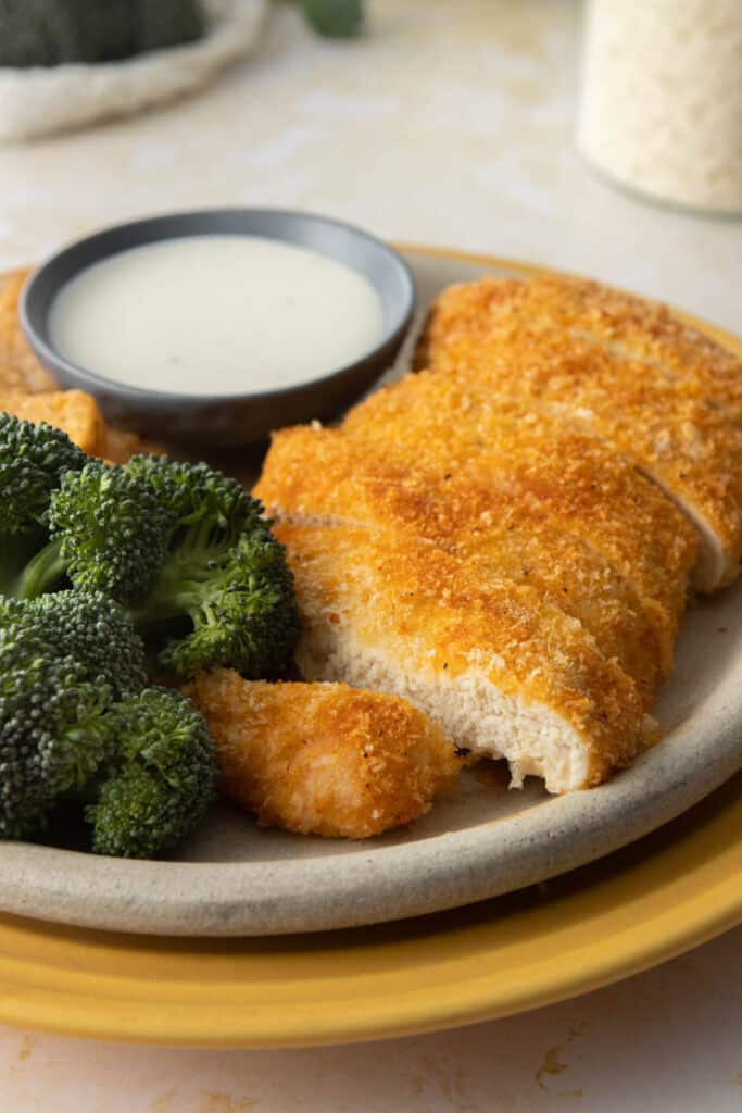 close up of sliced chicken breaded with panko crust, next to broccoli