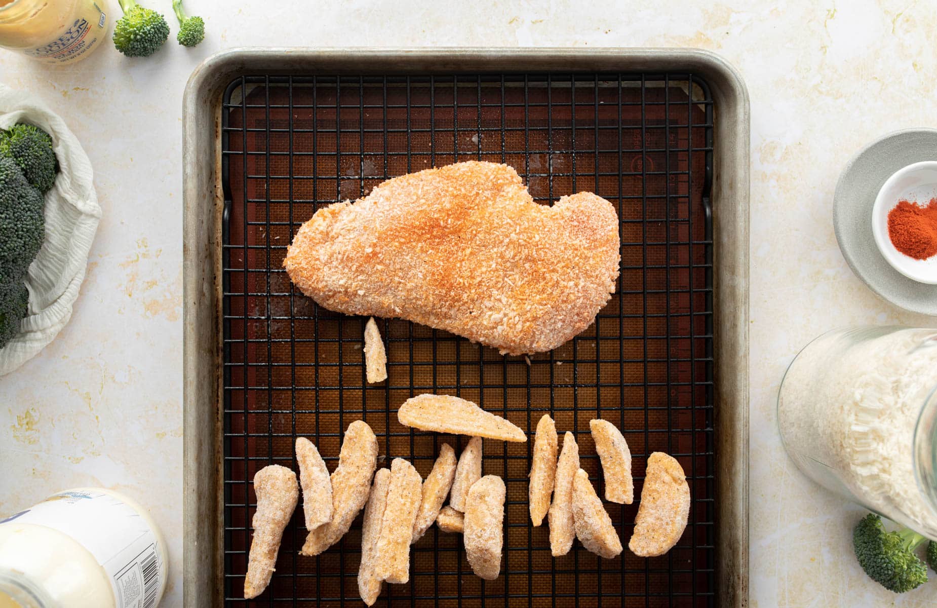 uncooked breaded chicken, potato wedges on baking sheet