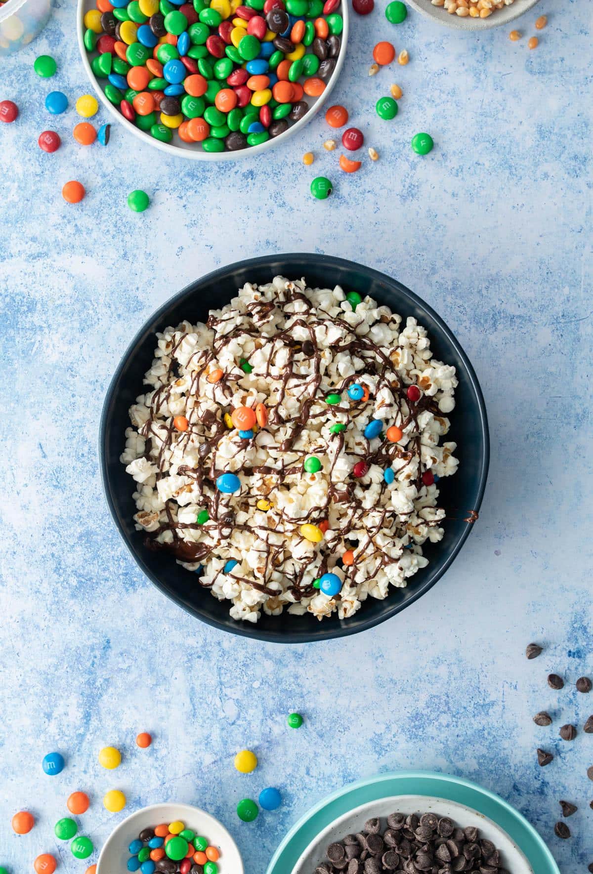 dark blue bowl with popcorn, m&ms, and chocolate drizzle in it