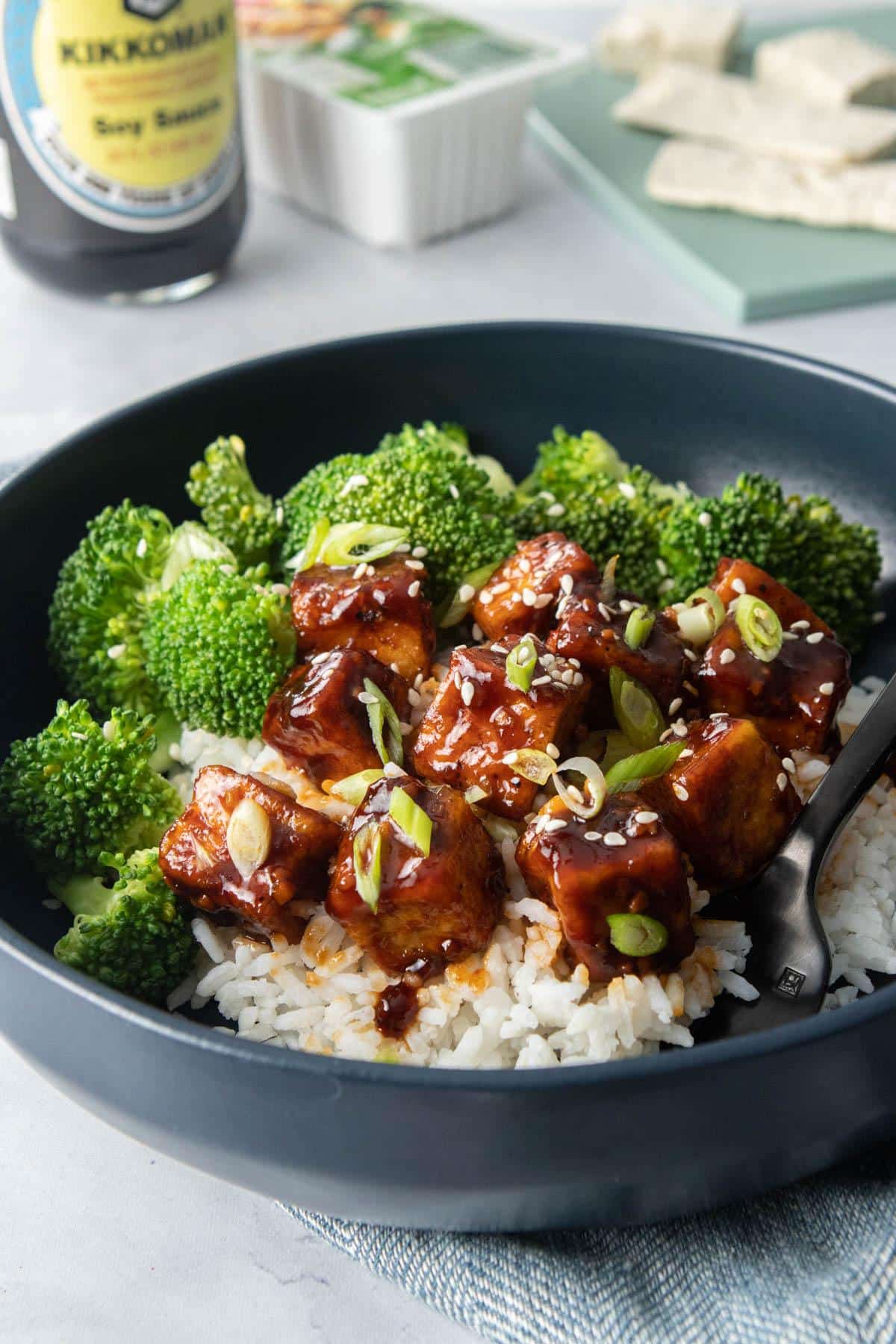 cubed tofu with thick soy sauce, broccoli over rice in blue bowl