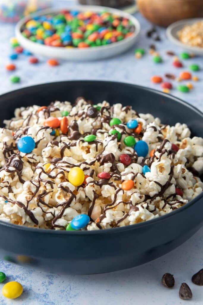 dark blue bowl filled with m&ms and chocolate drizzled over popcorn