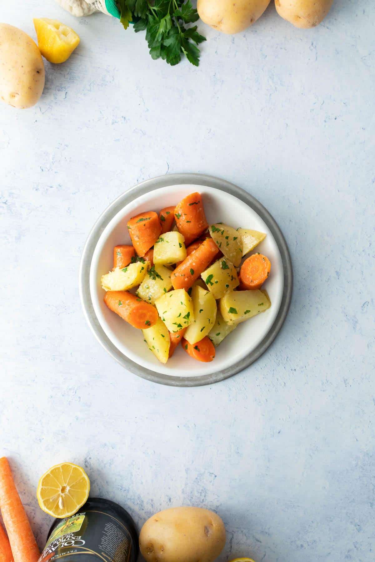 potatoes and carrots with herbs in white bowl with ingredients surrounding it