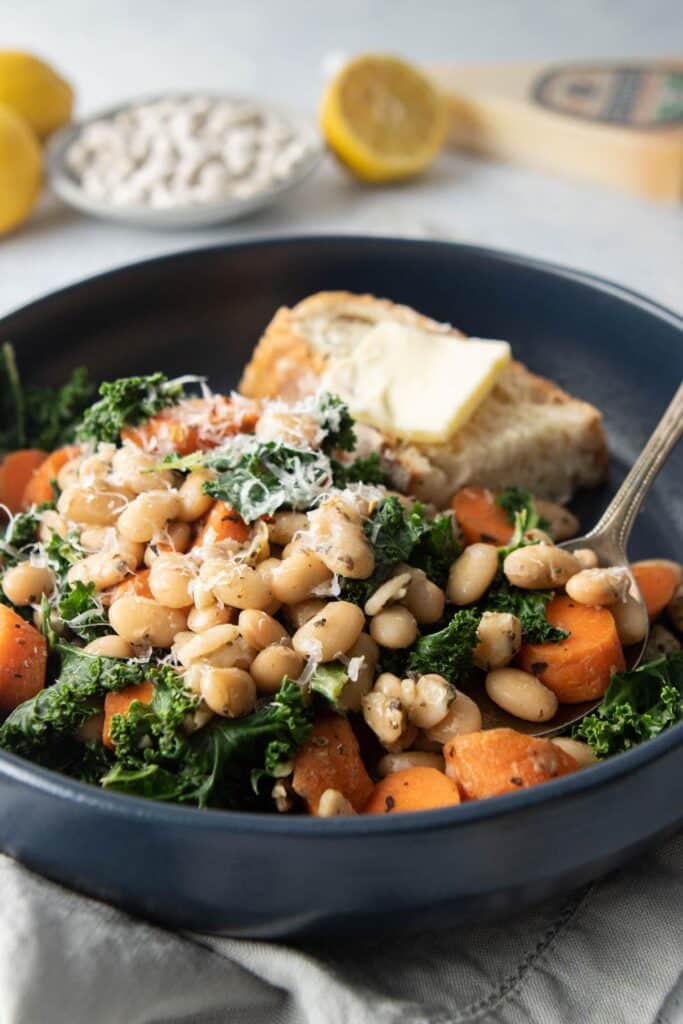 blue bowl with Italian beans, kale, carrots, and bread with butter