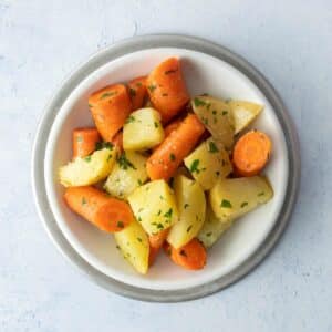 cut potatoes, carrots with herbs in white bowl
