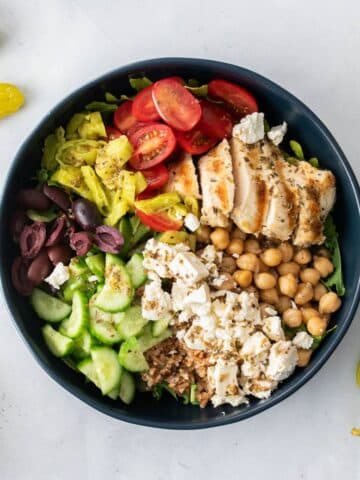 blue bowl full of vegetables, olives, grains, chickpeas, and chicken