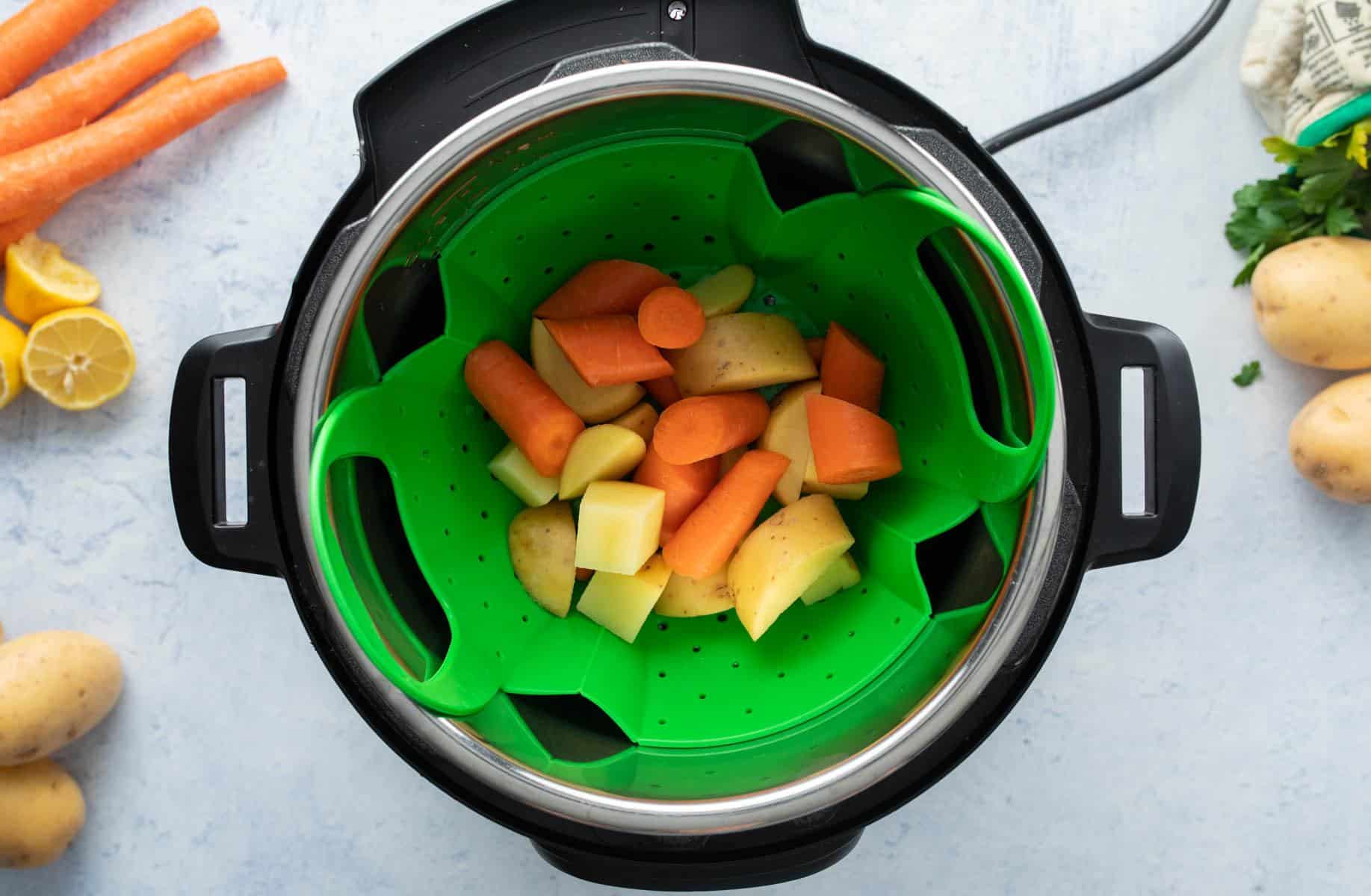 green steamer basket in Instant Pot with carrots, potatoes in it