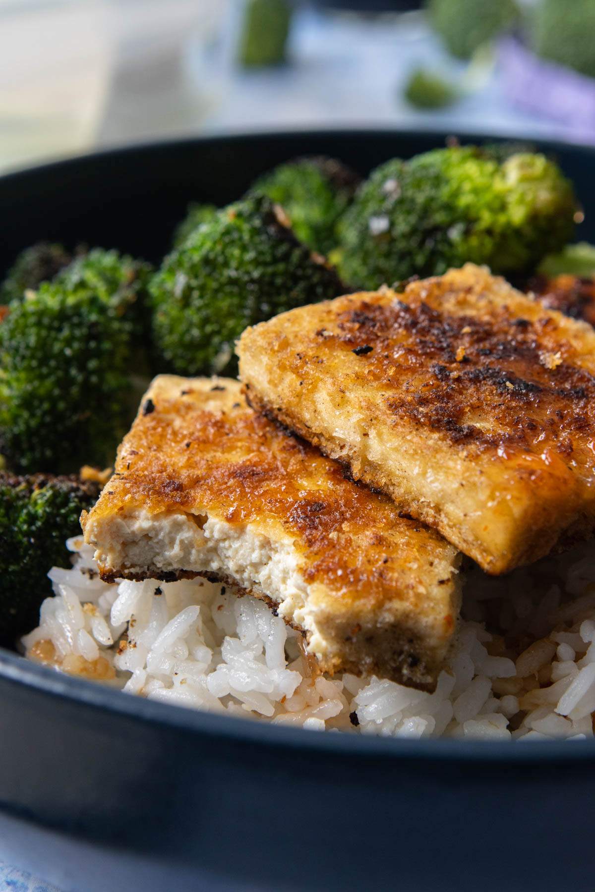 bite out of cooked tofu, with broccoli and rice in bowl