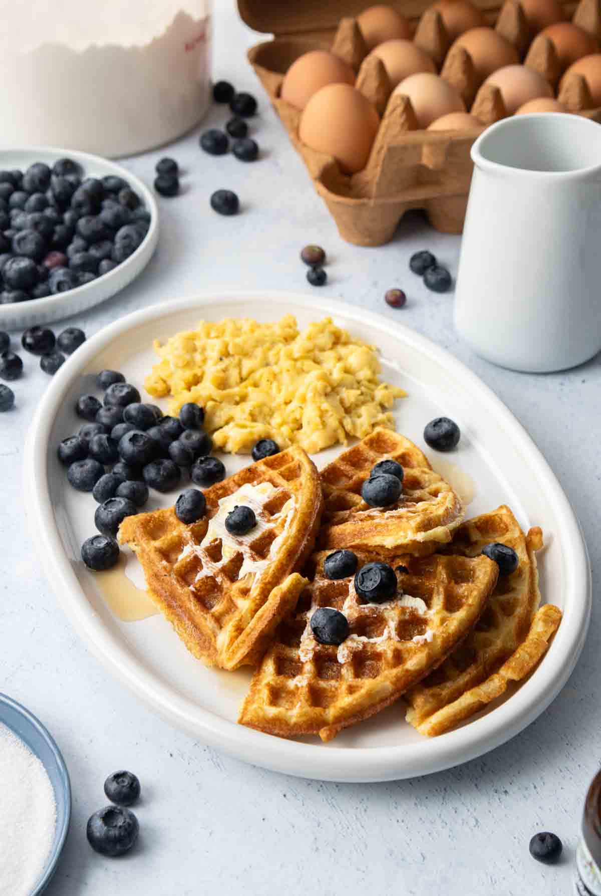 oval plate with waffle quarters, blueberries, and eggs on it