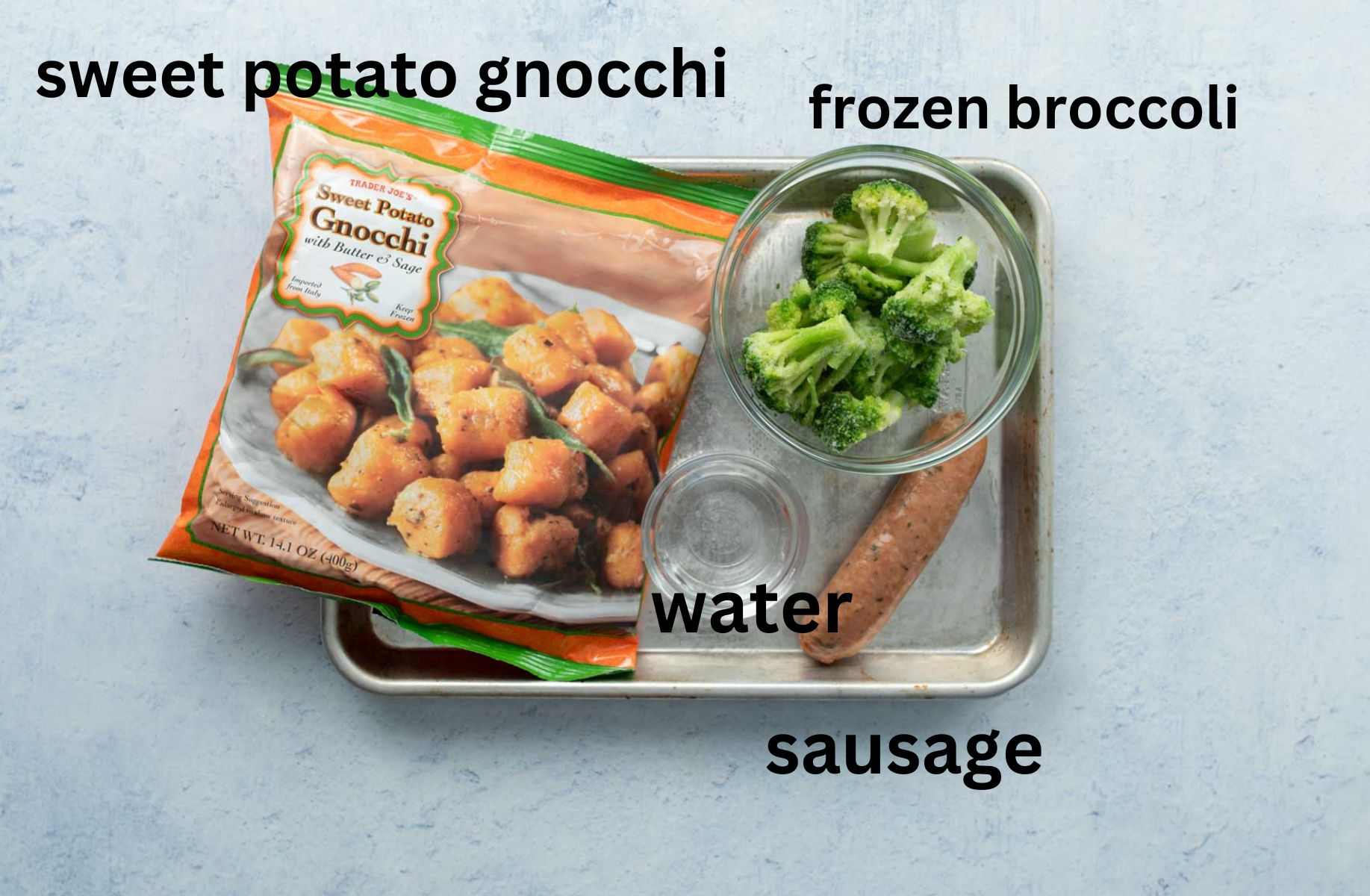 bag of sweet potato gnocchi, frozen broccoli, water, and sausage on baking sheet