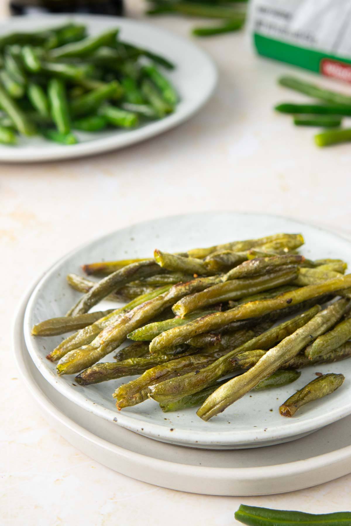 plate of roasted green beans with uncooked green beans behind