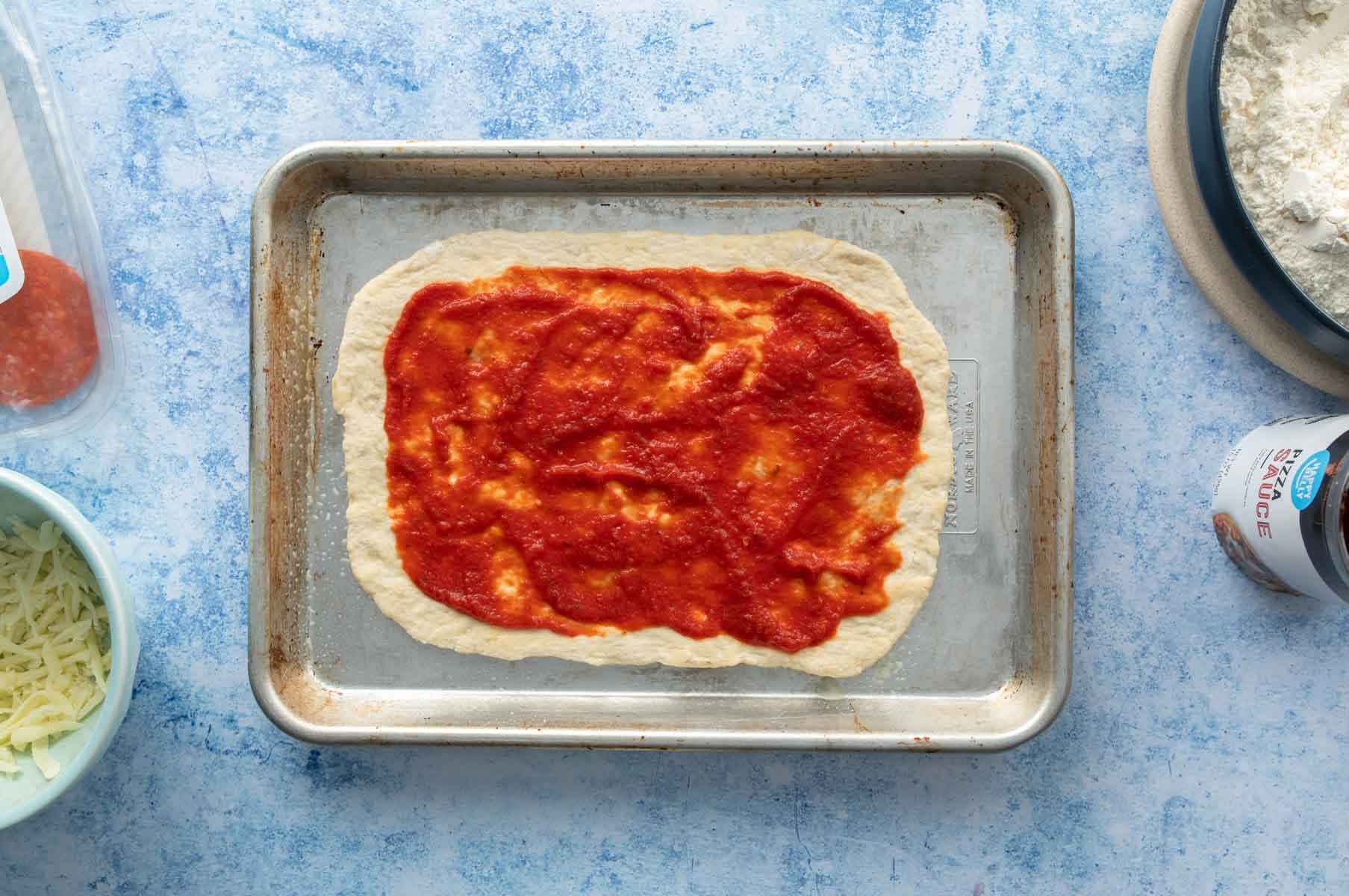 rectangular pizza dough with pizza sauce on it