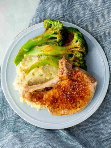blue plate with bone in pork chop, mashed potatoes, and broccoli on it